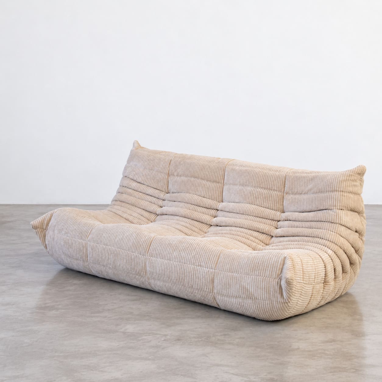 Sofa Togo 3-osobowa w beżowym sztruksie, ujęcie pod kątem ukazujące szerokie siedzisko oraz miękko zaokrąglone boki