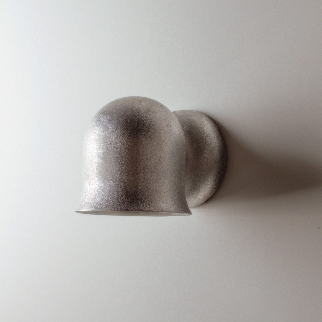 Kinkiet Convallaria z niepolerowanego aluminium zamontowany na jasnej ścianie.