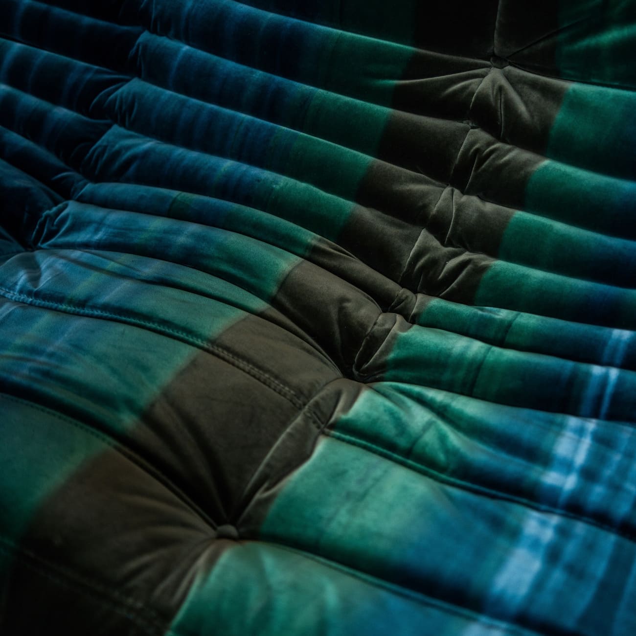 Zbliżenie velvet gradient dyeing blue na sofie Togo, przechodzące od głębokiego granatu do zieleni, z widocznymi fałdami pikowanej tapicerki