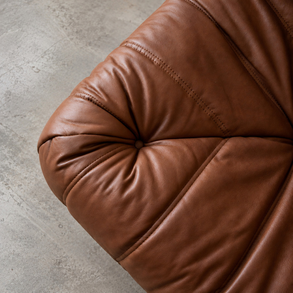 Pufa Togo vintage, detal narożnika siedziska w skórze Brown Leather Folk, z głębokim pikowaniem, guzikiem i naturalnymi fałdami skóry.